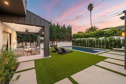 Modern backyard oasis with pool, lush greenery, and outdoor seating at sunset.